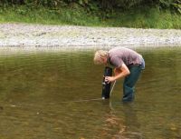 Figure 1. Measuring visual water clarity at a river site in the NRWQN. The technician is using an underwater periscope (black item in his left hand) fitted with a 45 degree mirror to view horizontally under the water surface. Visual clarity is the distance (measured by tape measure) at which the visual target (black disc on the left of the image) disappears. The black disc is fixed to a steel pole driven into the river gravel. Image - Graham Timpany.